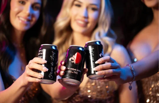 Three women holding Fleur de Leaf’s THC root beer up and posing.